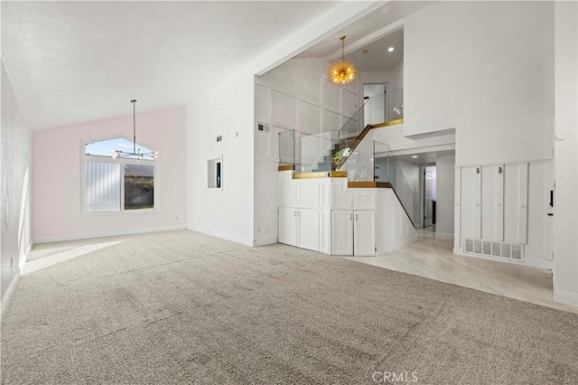 unfurnished living room with light carpet, high vaulted ceiling, and a chandelier