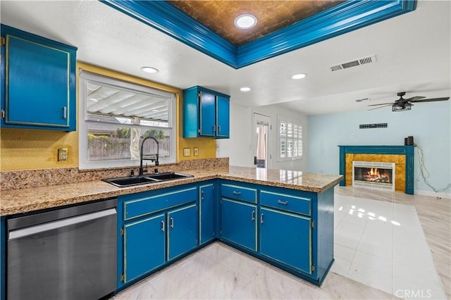 kitchen featuring ceiling fan, sink, blue cabinetry, dishwasher, and a tiled fireplace