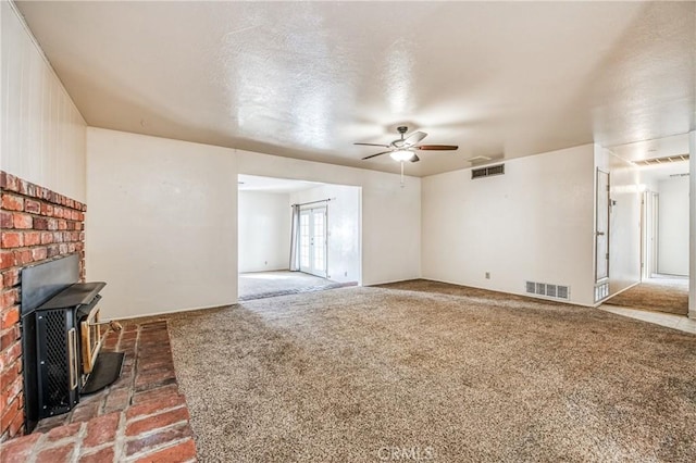 unfurnished living room with a textured ceiling, ceiling fan, a wood stove, and carpet floors