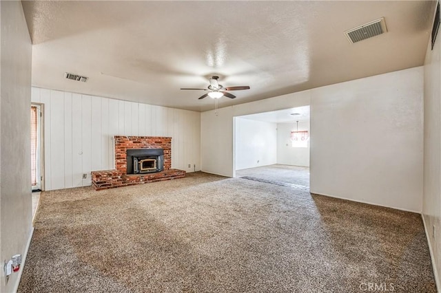 unfurnished living room with carpet flooring, a textured ceiling, ceiling fan, wooden walls, and a wood stove