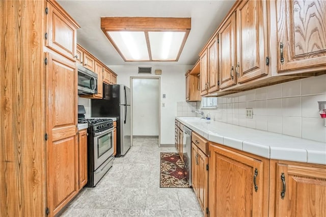 kitchen featuring decorative backsplash, stainless steel appliances, tile counters, and sink