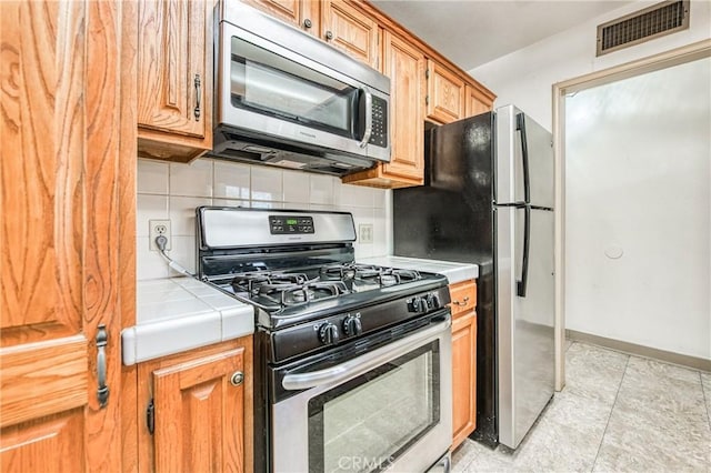 kitchen featuring tile countertops, appliances with stainless steel finishes, tasteful backsplash, and light tile patterned floors