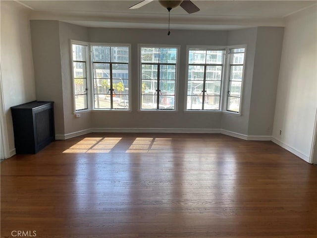 empty room featuring a wealth of natural light, a ceiling fan, and dark wood-style floors