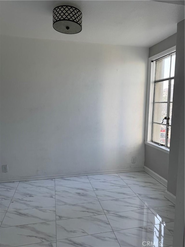 unfurnished room with plenty of natural light, marble finish floor, and baseboards