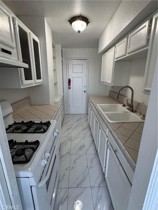 kitchen featuring white gas range, marble finish floor, tile countertops, and a sink