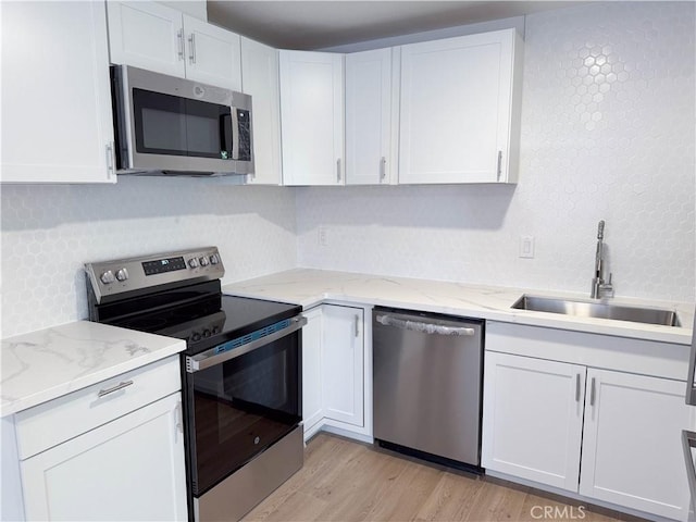 kitchen with sink, light stone countertops, appliances with stainless steel finishes, light hardwood / wood-style floors, and white cabinetry