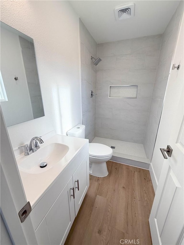 bathroom with hardwood / wood-style flooring, vanity, toilet, and a tile shower