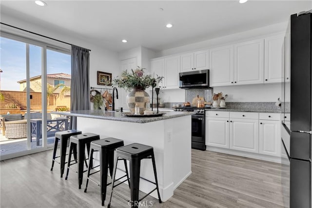 kitchen with white cabinetry, stainless steel appliances, light hardwood / wood-style flooring, an island with sink, and a kitchen bar