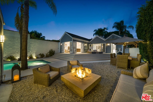 back house at dusk with a fenced in pool, a patio area, and an outdoor fire pit