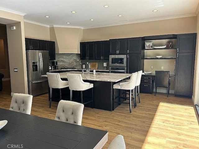 kitchen featuring a kitchen bar, appliances with stainless steel finishes, light stone countertops, a center island with sink, and light hardwood / wood-style floors