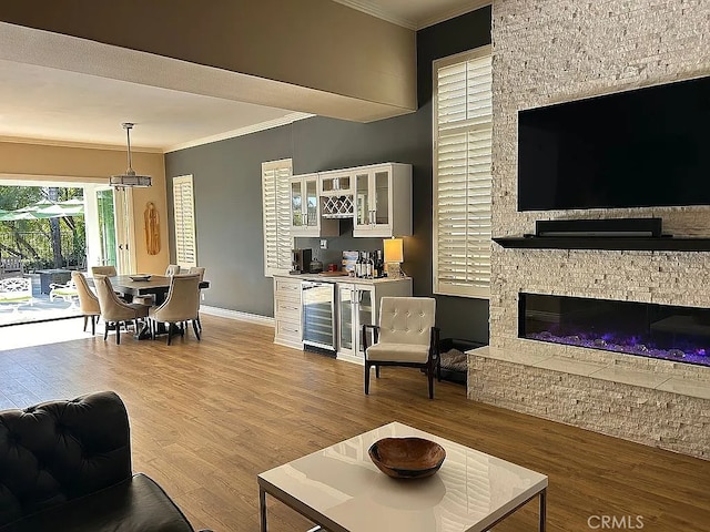 living room with light hardwood / wood-style floors, a stone fireplace, ornamental molding, and beverage cooler