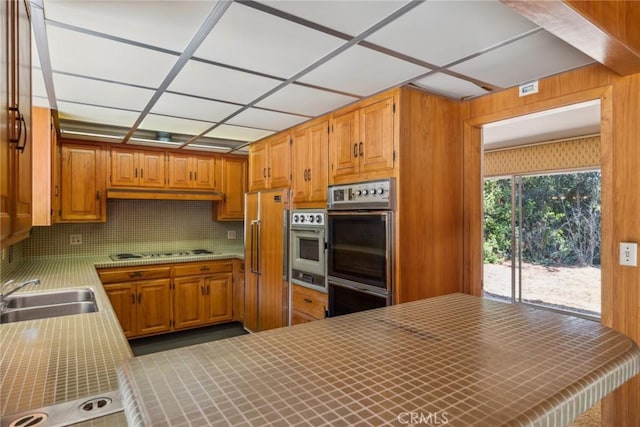 kitchen featuring sink, stainless steel double oven, white gas cooktop, kitchen peninsula, and wooden walls