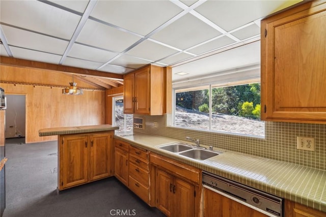 kitchen with wood walls, sink, stainless steel dishwasher, decorative backsplash, and kitchen peninsula