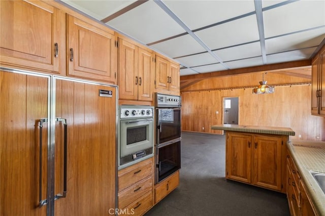 kitchen featuring dark colored carpet, hanging light fixtures, wooden walls, paneled built in refrigerator, and stainless steel double oven