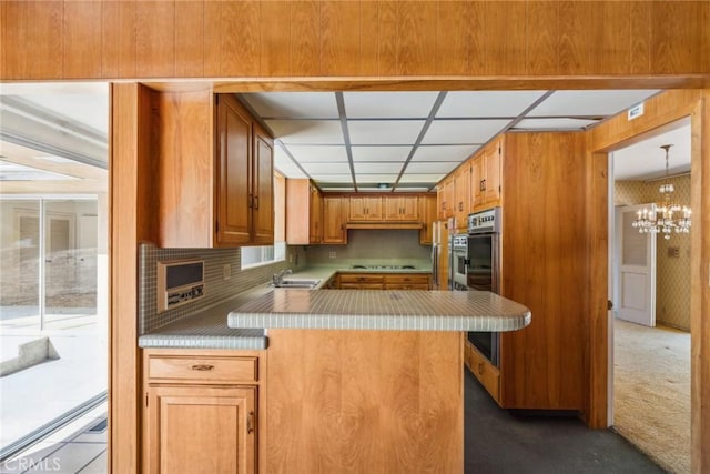 kitchen with sink, kitchen peninsula, stovetop, a chandelier, and carpet