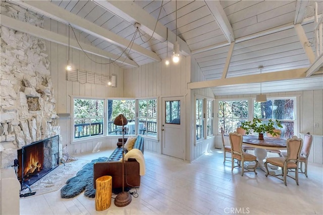 living room featuring beam ceiling, light hardwood / wood-style flooring, high vaulted ceiling, wood walls, and a fireplace