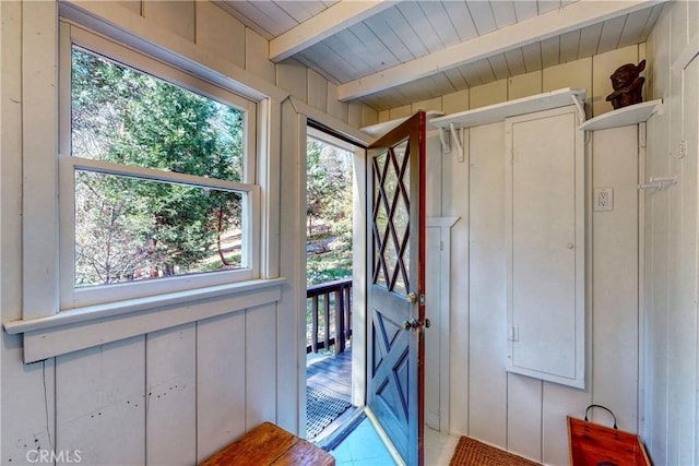 doorway to outside with beam ceiling, wooden walls, and a healthy amount of sunlight