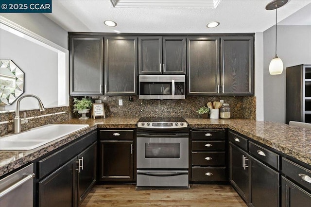 kitchen featuring decorative light fixtures, stainless steel appliances, dark stone countertops, sink, and backsplash