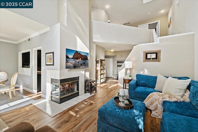 living room with a tile fireplace, crown molding, a towering ceiling, and light wood-type flooring