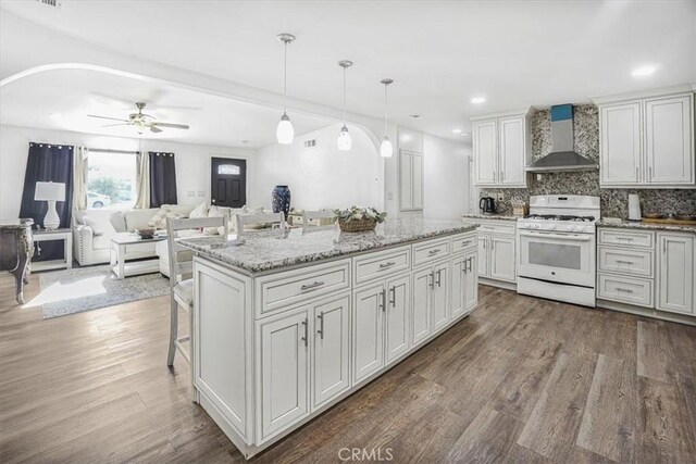 kitchen featuring dark hardwood / wood-style floors, white range with gas cooktop, pendant lighting, wall chimney exhaust hood, and white cabinets