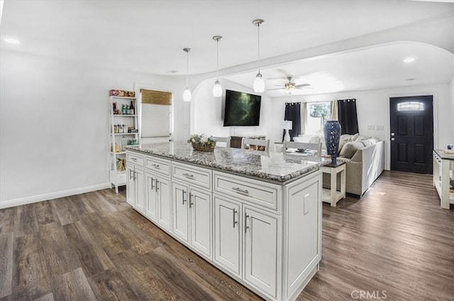 kitchen featuring ceiling fan, white cabinets, hanging light fixtures, a kitchen island, and light stone counters