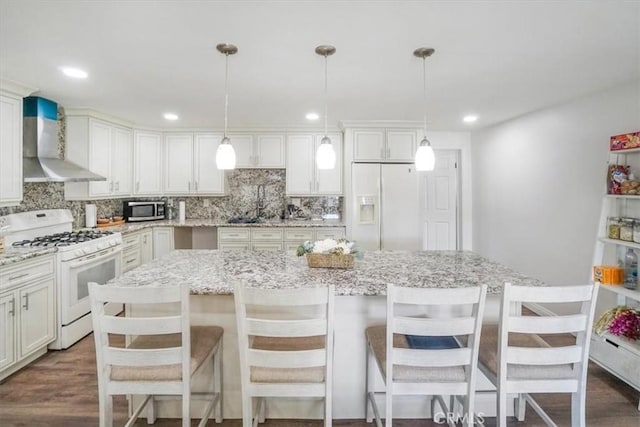 kitchen featuring a center island, wall chimney exhaust hood, white appliances, and pendant lighting