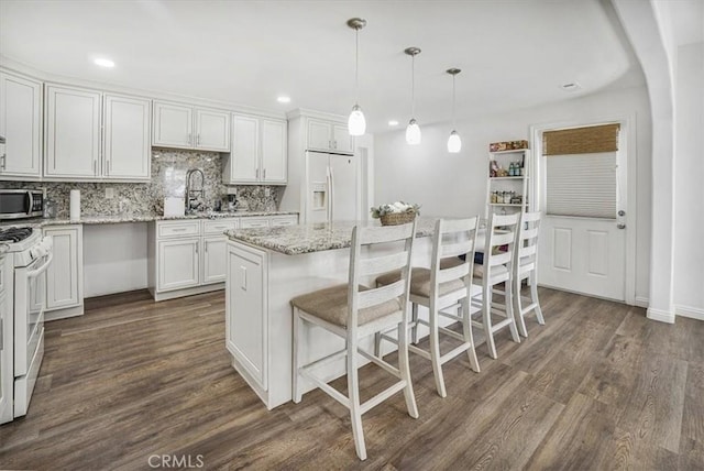 kitchen featuring white appliances, white cabinets, a kitchen island, decorative light fixtures, and dark hardwood / wood-style floors