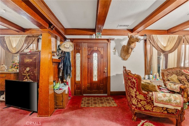 carpeted entrance foyer with beam ceiling, ornate columns, and a textured ceiling