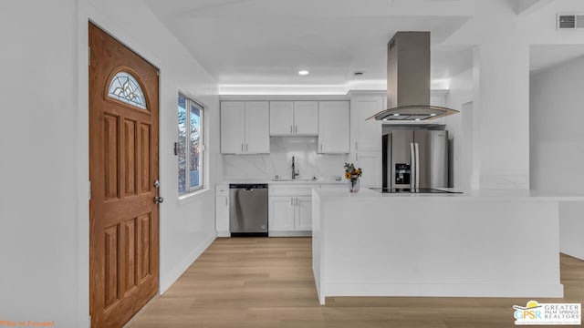 kitchen with appliances with stainless steel finishes, sink, white cabinets, island exhaust hood, and decorative backsplash