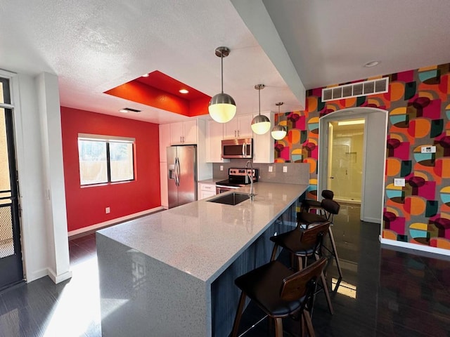 kitchen with kitchen peninsula, decorative light fixtures, light stone counters, white cabinetry, and stainless steel appliances