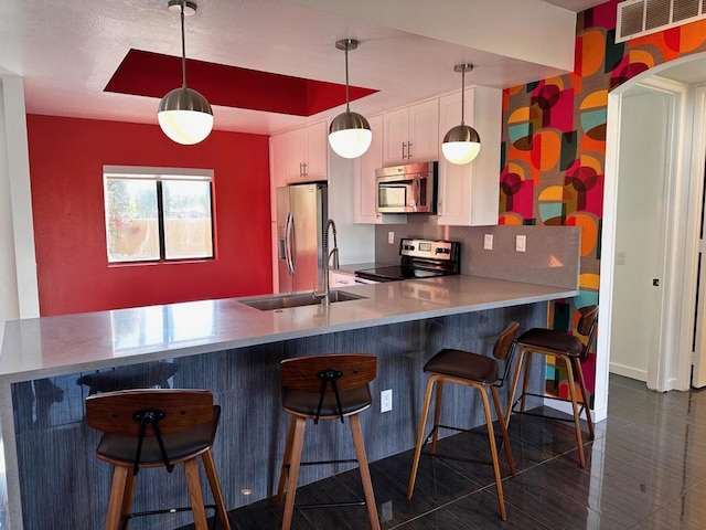 kitchen with decorative light fixtures, a kitchen bar, white cabinetry, and stainless steel appliances