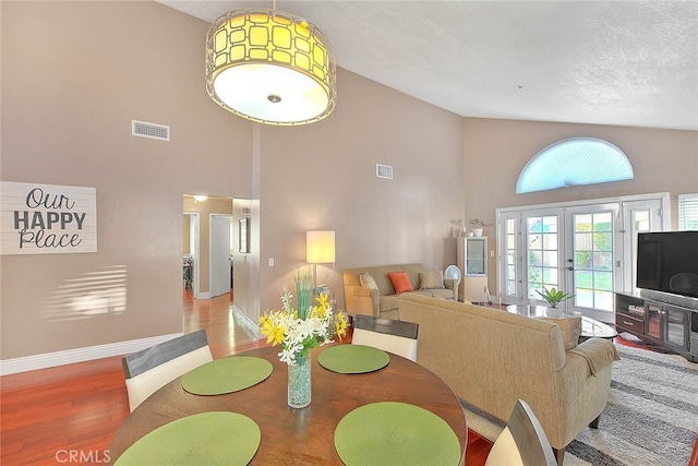 dining room featuring a high ceiling, a textured ceiling, french doors, and wood-type flooring