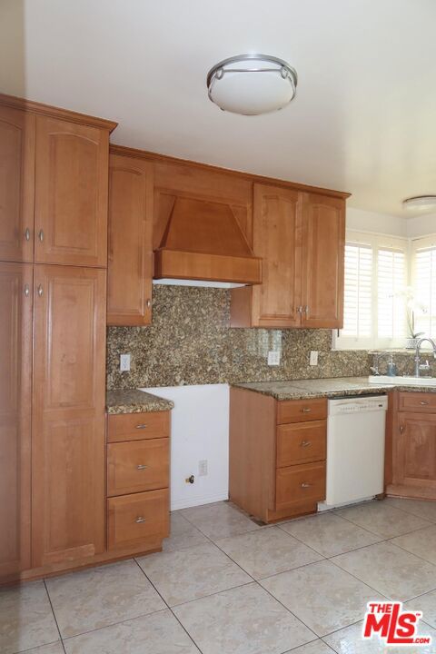 kitchen featuring white dishwasher, sink, tasteful backsplash, light tile patterned flooring, and custom range hood