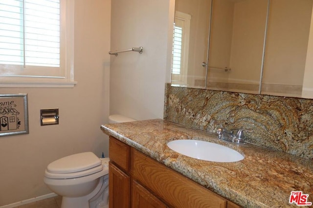 bathroom featuring decorative backsplash, a healthy amount of sunlight, toilet, and vanity