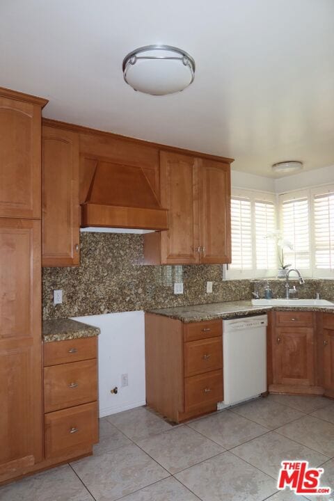 kitchen featuring dishwasher, premium range hood, sink, light tile patterned floors, and light stone counters