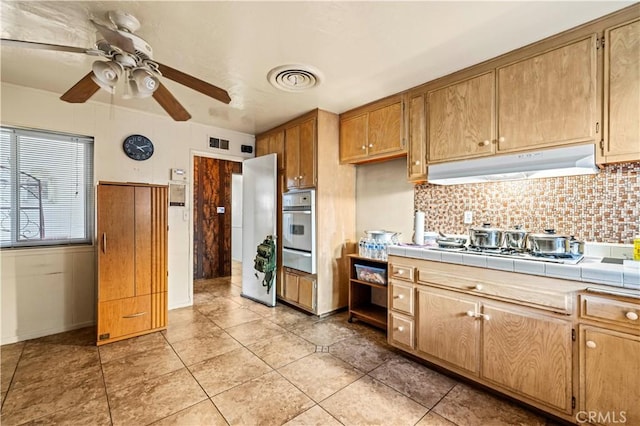 kitchen with tasteful backsplash, stainless steel oven, ceiling fan, tile countertops, and light tile patterned flooring