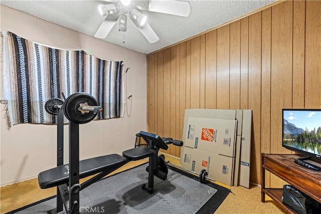 workout area with light carpet, a textured ceiling, ceiling fan, and wood walls