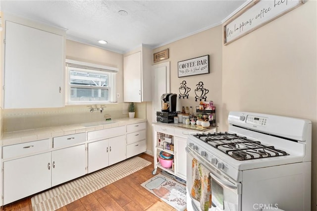 kitchen featuring sink, gas range gas stove, white cabinetry, light hardwood / wood-style flooring, and tile counters