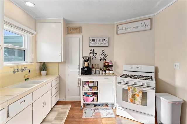 kitchen with tile countertops, white gas range, sink, white cabinets, and light hardwood / wood-style flooring