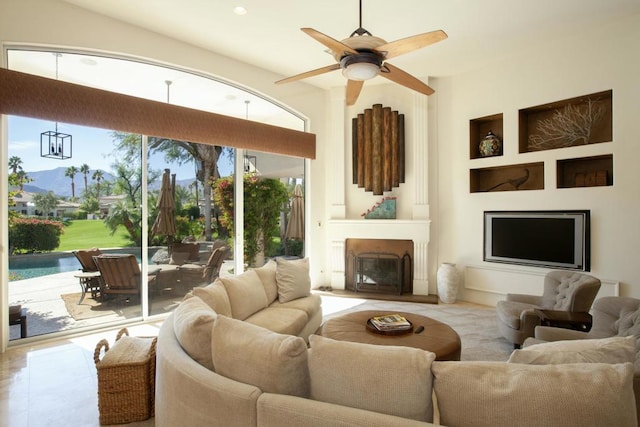 tiled living room with ceiling fan, a large fireplace, and built in shelves