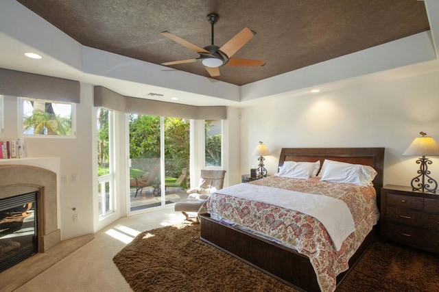 carpeted bedroom with multiple windows, access to outside, a raised ceiling, and ceiling fan