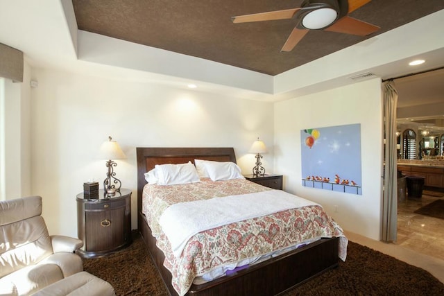 bedroom with a raised ceiling, ceiling fan, and ensuite bathroom