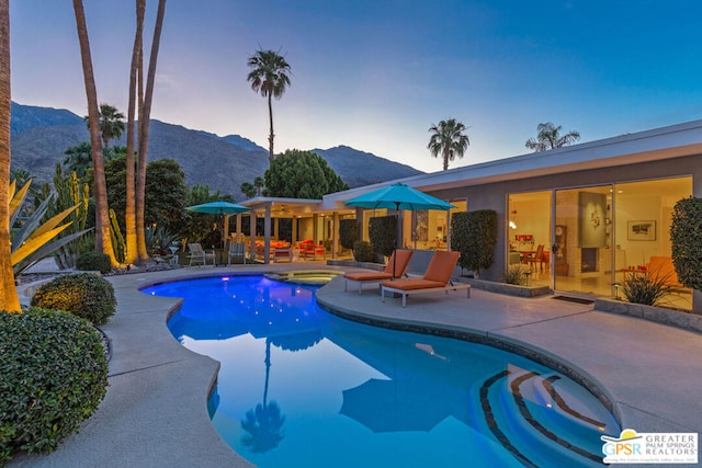 pool at dusk featuring a patio area, a mountain view, and an in ground hot tub