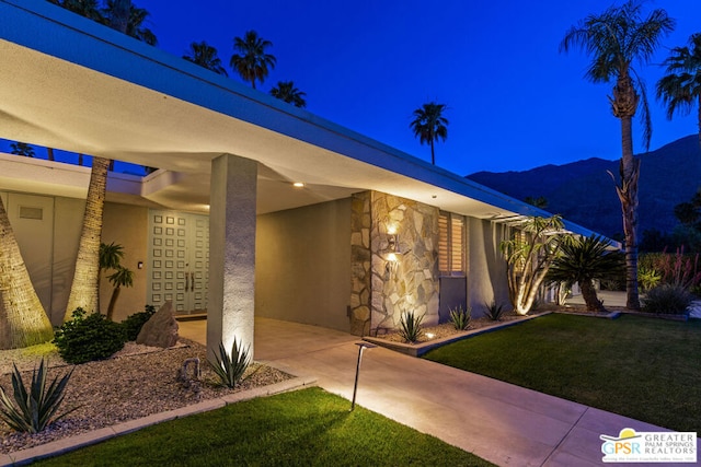 exterior entry at twilight with a mountain view and a yard