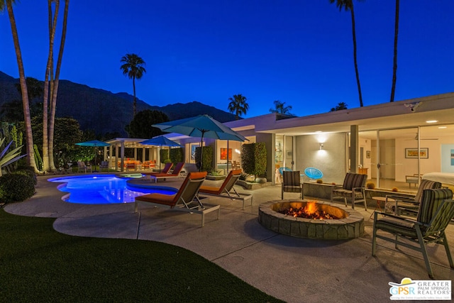 pool at twilight featuring a mountain view, a patio area, and an outdoor fire pit