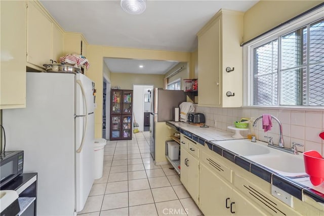 kitchen featuring sink, tile countertops, white fridge, decorative backsplash, and light tile patterned flooring