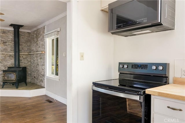 kitchen featuring appliances with stainless steel finishes, a wood stove, dark wood-type flooring, and crown molding