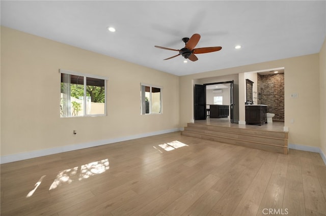 unfurnished living room with light wood-type flooring, a wood stove, and ceiling fan