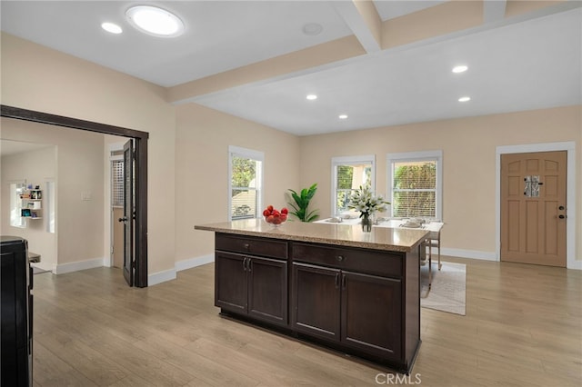 kitchen with light stone countertops, dark brown cabinetry, beam ceiling, light hardwood / wood-style flooring, and a center island