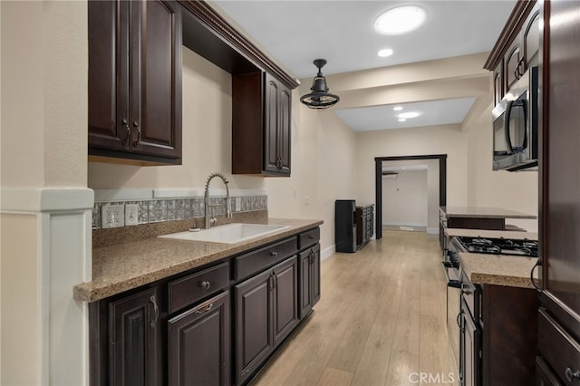 kitchen featuring dark brown cabinetry, sink, hanging light fixtures, stainless steel appliances, and light wood-type flooring